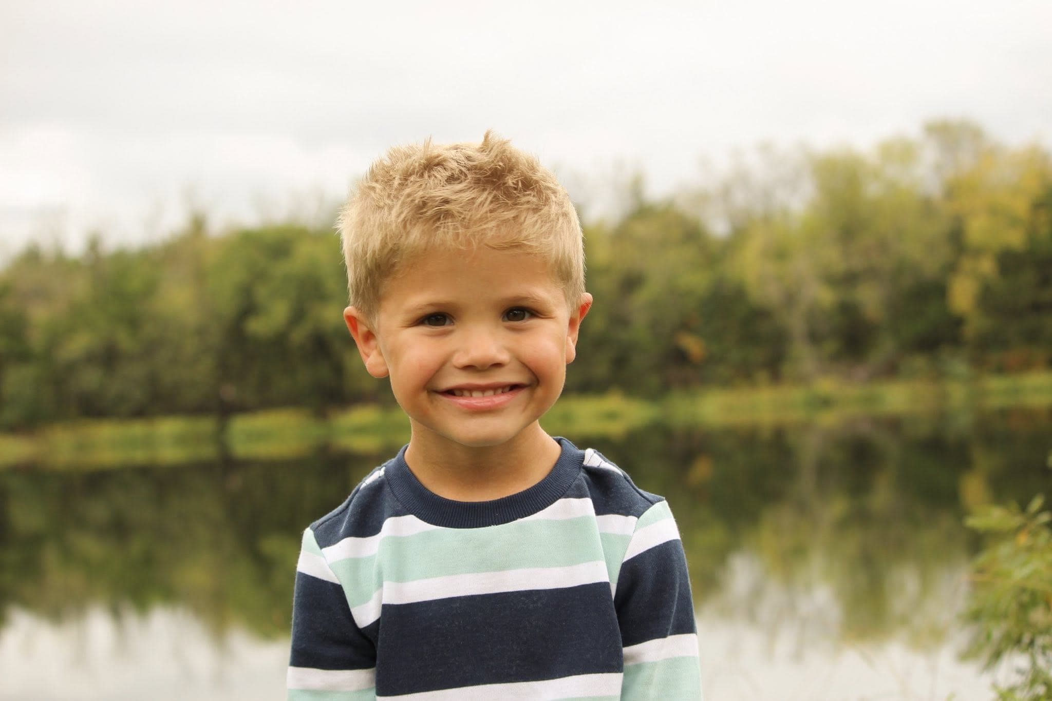 Smiling boy in a striped shirt beside a calm pond
