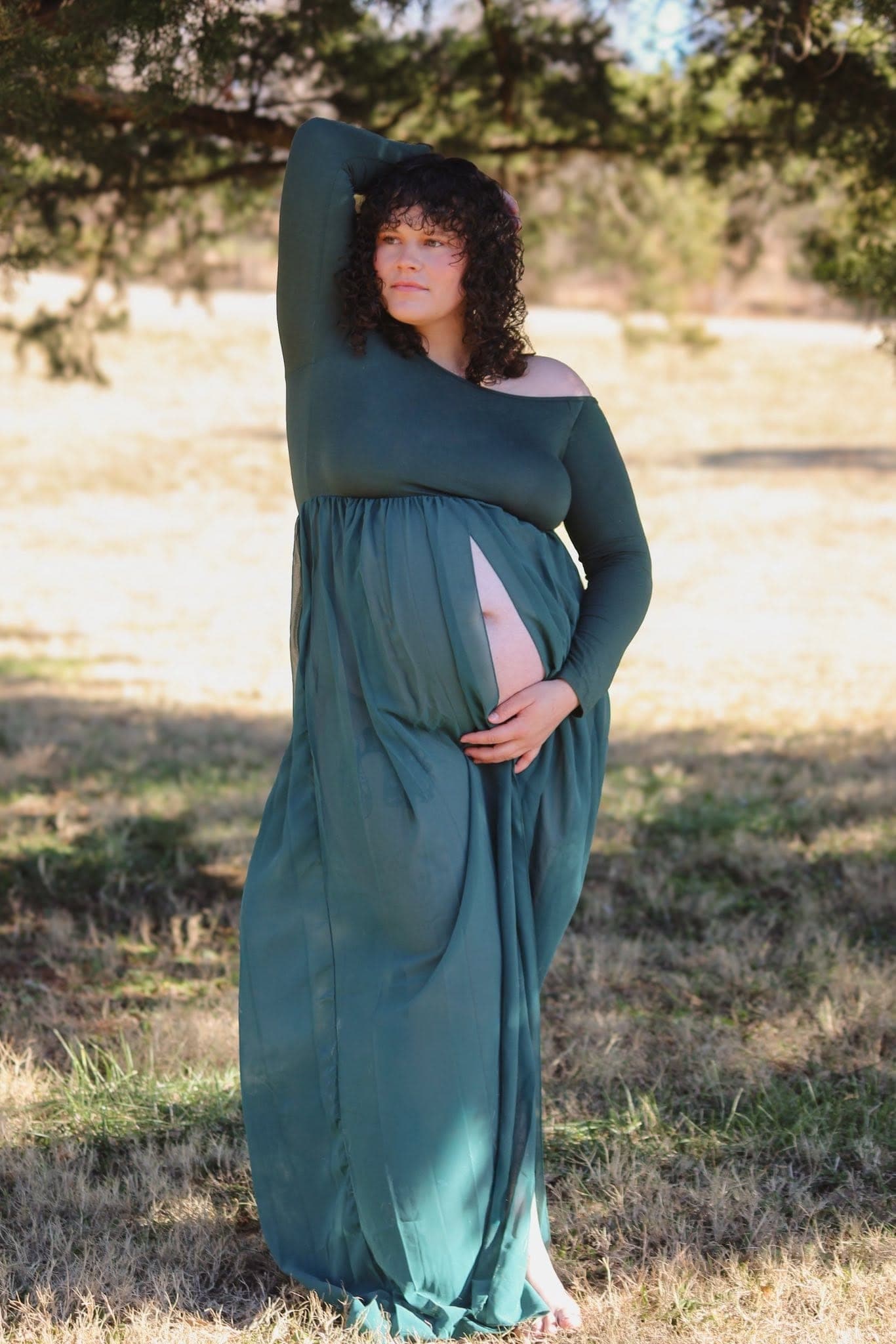 Mom-to-be in a flowing green dress cradling her bump in a sunny field