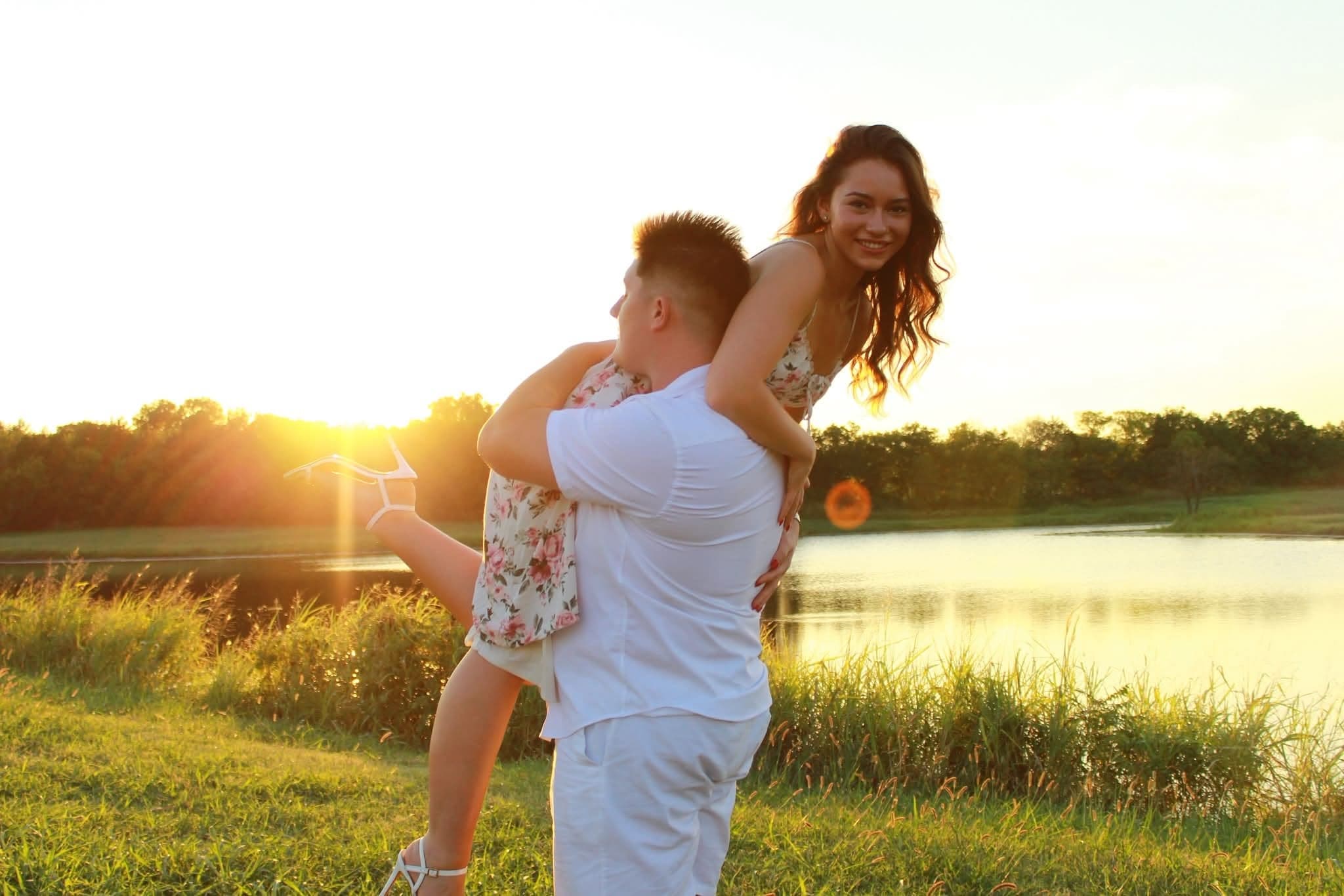 Couple laughing as he lifts her at golden hour beside a pond