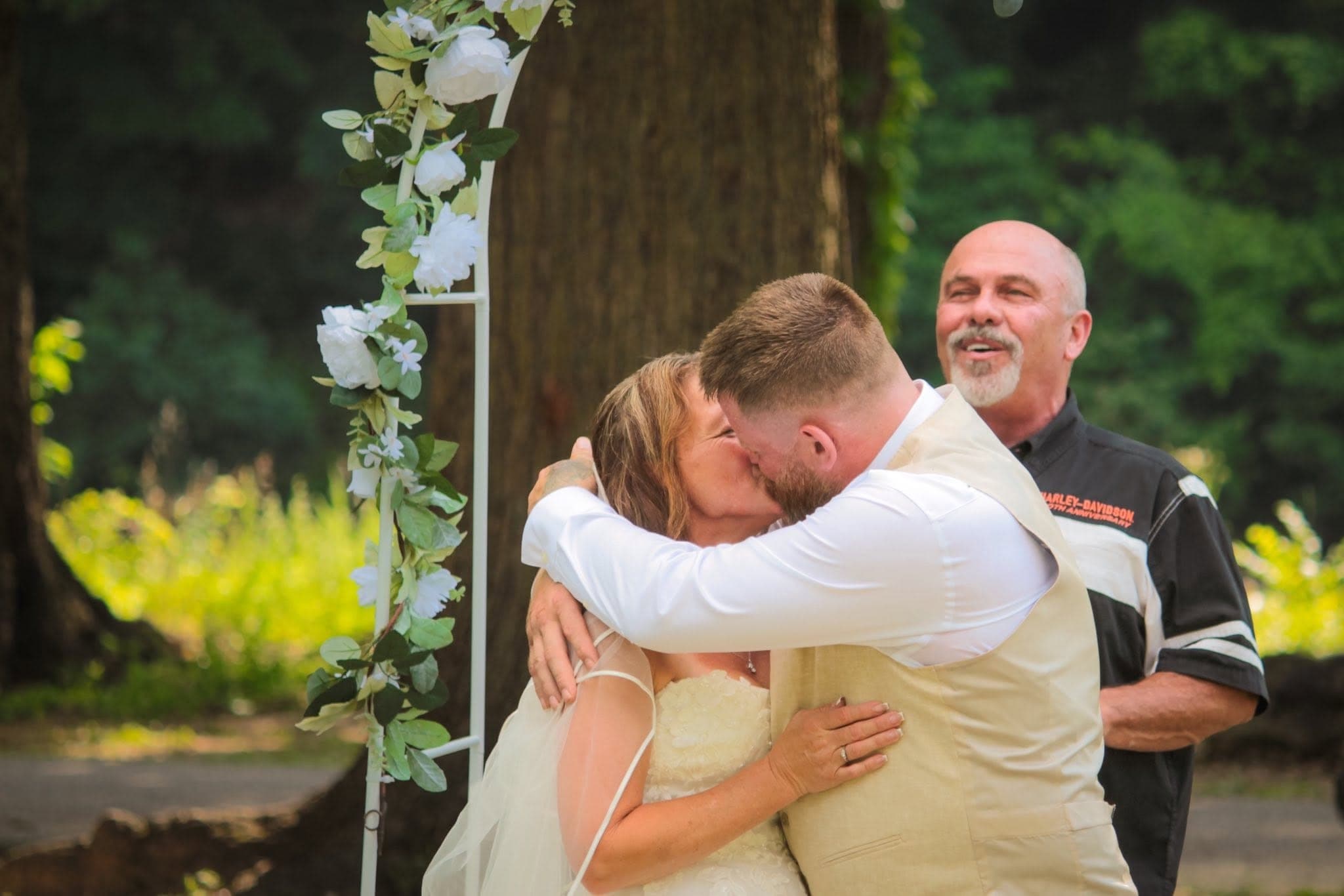 Bride and groom share their first kiss under a floral arch